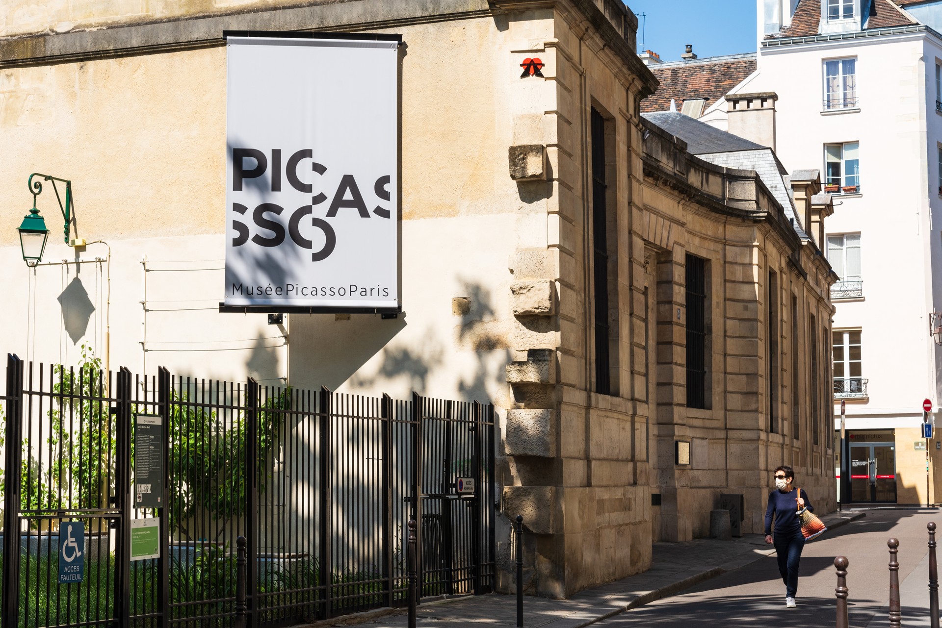 Woman in protective mask walking near closed Picasso museum in Marais quarter at empty street. Covid-19 lockdown lifestyle.